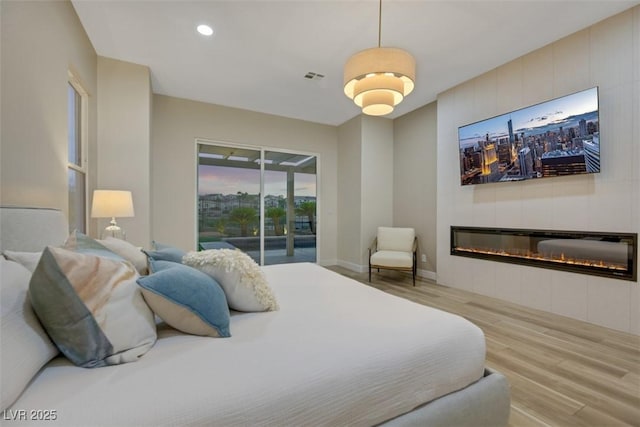 bedroom featuring a tiled fireplace, access to exterior, and light hardwood / wood-style flooring