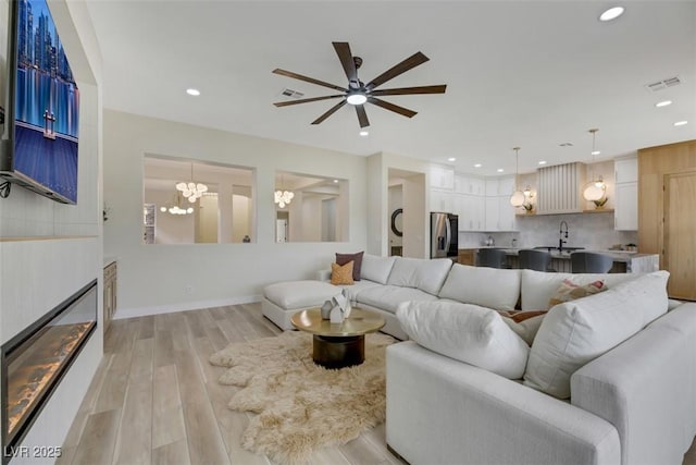 living room with sink, ceiling fan with notable chandelier, and light hardwood / wood-style floors