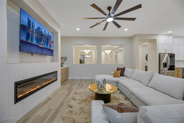 living room with ceiling fan with notable chandelier, a tile fireplace, and light hardwood / wood-style flooring