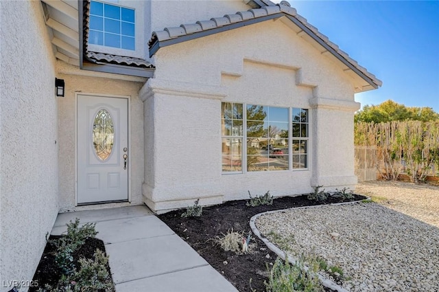 doorway to property featuring a tile roof, fence, and stucco siding