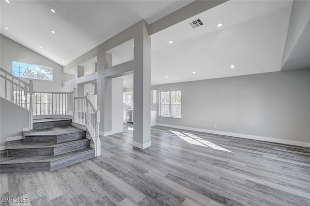 unfurnished living room with visible vents, baseboards, stairway, light wood-style floors, and high vaulted ceiling