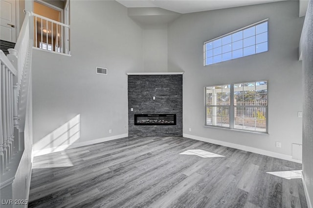 unfurnished living room with wood finished floors, a towering ceiling, visible vents, baseboards, and a glass covered fireplace