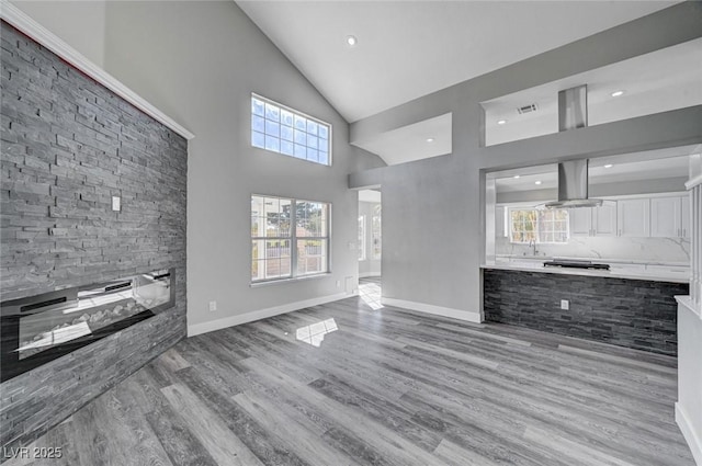 unfurnished living room with high vaulted ceiling, light wood-type flooring, visible vents, and baseboards