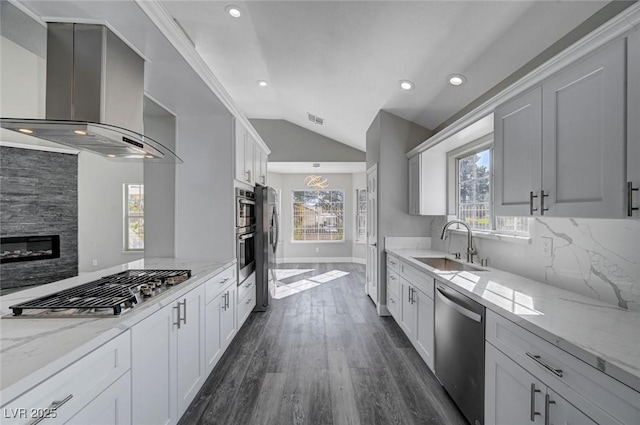 kitchen with light stone countertops, wall chimney exhaust hood, appliances with stainless steel finishes, and a sink