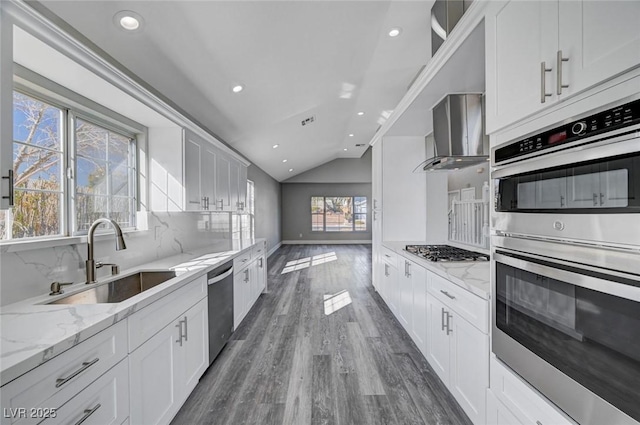 kitchen featuring wall chimney range hood, appliances with stainless steel finishes, a sink, and white cabinetry