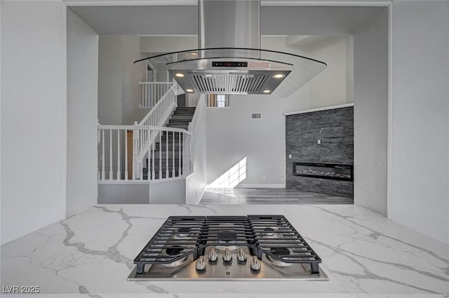 interior space featuring marble finish floor, visible vents, stainless steel gas stovetop, a glass covered fireplace, and light stone countertops