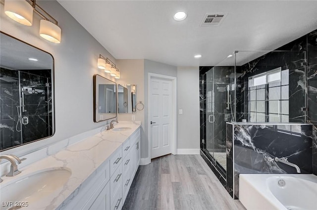 bathroom featuring visible vents, a sink, a marble finish shower, and wood finished floors