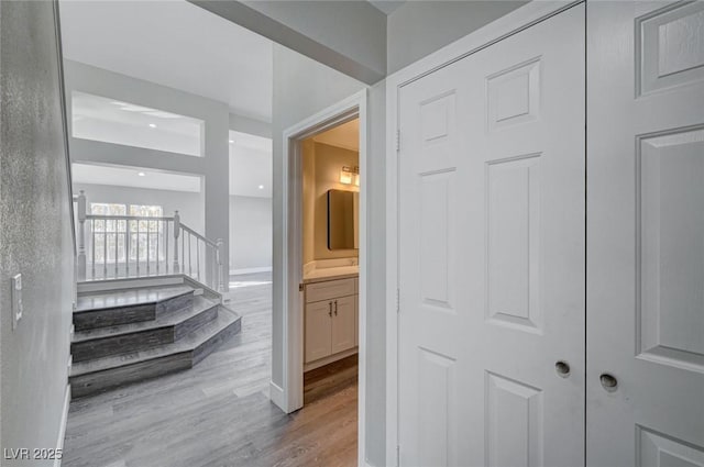 corridor featuring light wood-type flooring, baseboards, and stairs