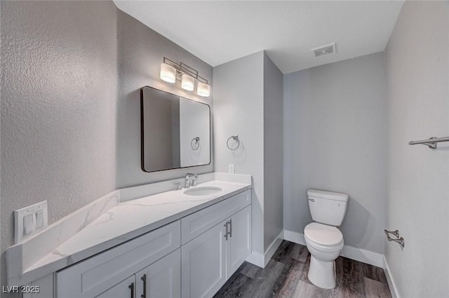 bathroom with visible vents, toilet, vanity, wood finished floors, and baseboards