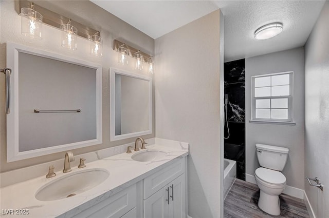 full bath featuring toilet, double vanity, a textured ceiling, and a sink