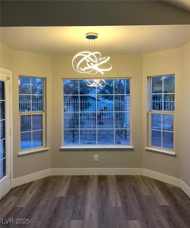 unfurnished dining area featuring dark wood finished floors, baseboards, and an inviting chandelier