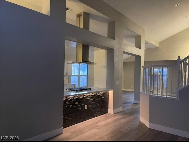 kitchen featuring baseboards, wood finished floors, a high ceiling, extractor fan, and stainless steel gas cooktop