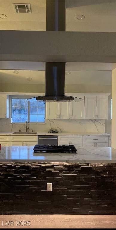 kitchen featuring island exhaust hood, tasteful backsplash, light countertops, visible vents, and a sink