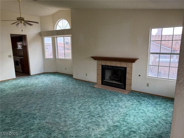 unfurnished living room with high vaulted ceiling, a tile fireplace, ceiling fan, and carpet