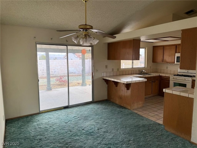 kitchen featuring tile counters, a textured ceiling, white gas range, vaulted ceiling, and kitchen peninsula