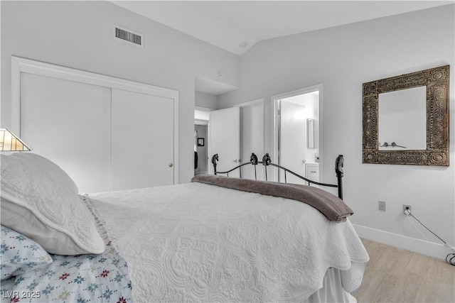 bedroom featuring connected bathroom, vaulted ceiling, a closet, and light hardwood / wood-style flooring