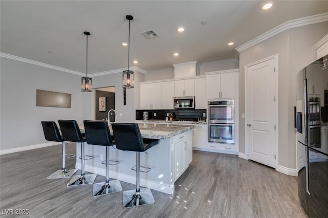 kitchen with appliances with stainless steel finishes, light stone counters, tasteful backsplash, an island with sink, and white cabinets