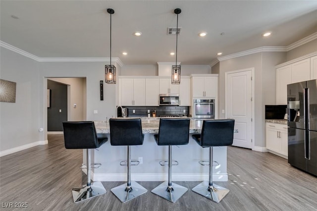 kitchen with appliances with stainless steel finishes, pendant lighting, tasteful backsplash, white cabinets, and a kitchen island with sink