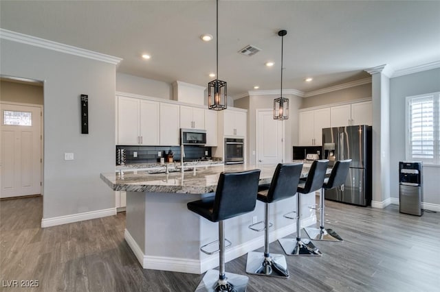 kitchen featuring a kitchen island with sink, backsplash, white cabinetry, stainless steel appliances, and light stone countertops