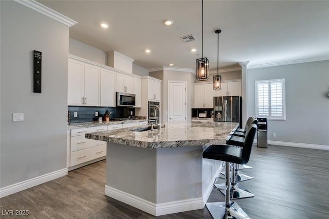 kitchen with appliances with stainless steel finishes, white cabinetry, a kitchen bar, decorative backsplash, and a spacious island