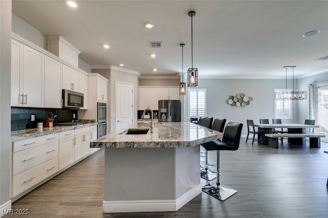 kitchen with appliances with stainless steel finishes, a kitchen island with sink, and white cabinets