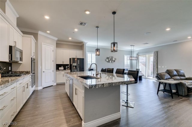 kitchen featuring a breakfast bar, an island with sink, white cabinetry, sink, and stainless steel appliances