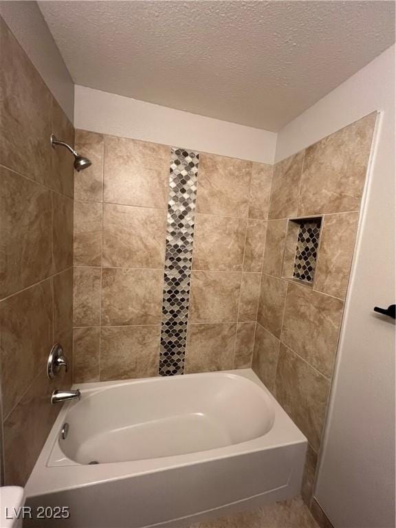 bathroom with a textured ceiling, toilet, and tiled shower / bath