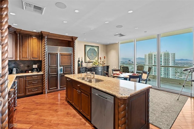 kitchen with an island with sink, sink, a wall of windows, stainless steel dishwasher, and paneled refrigerator