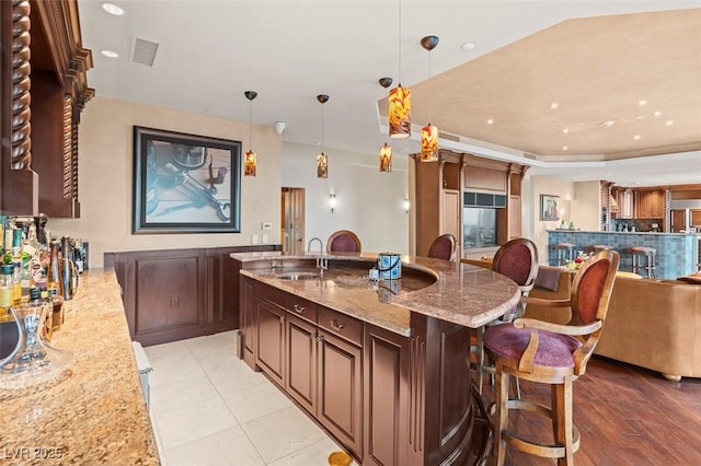 kitchen featuring pendant lighting, sink, a kitchen bar, light tile patterned floors, and light stone counters