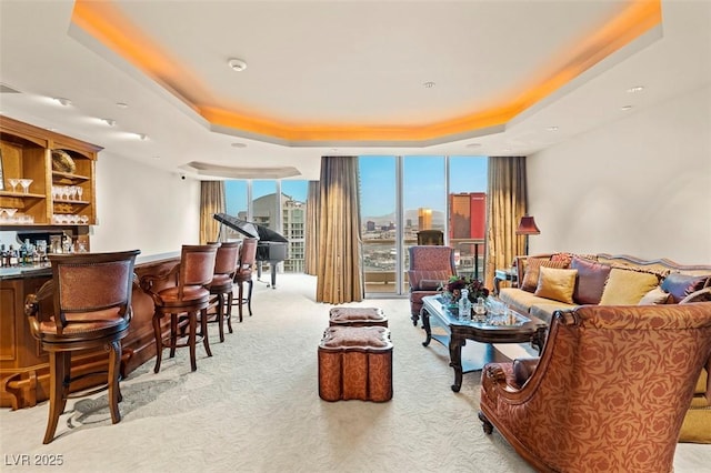 carpeted living room with a raised ceiling, floor to ceiling windows, and bar