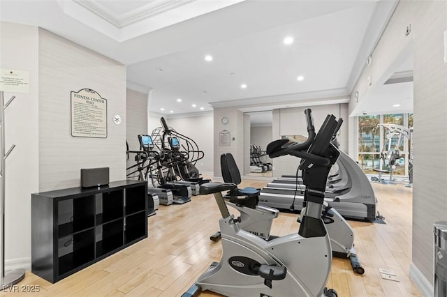 workout area featuring ornamental molding, a raised ceiling, and light wood-type flooring