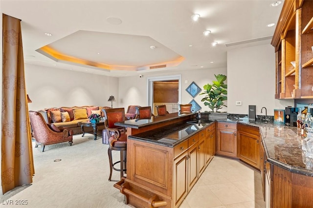 kitchen featuring a raised ceiling, sink, a kitchen breakfast bar, and kitchen peninsula