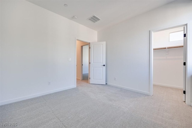 unfurnished bedroom with a walk in closet, light colored carpet, and a closet