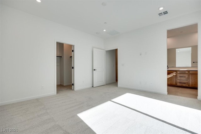 unfurnished bedroom with a walk in closet, connected bathroom, and light carpet