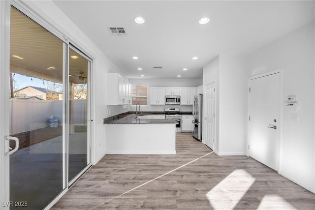 kitchen featuring sink, appliances with stainless steel finishes, kitchen peninsula, white cabinets, and dark stone counters