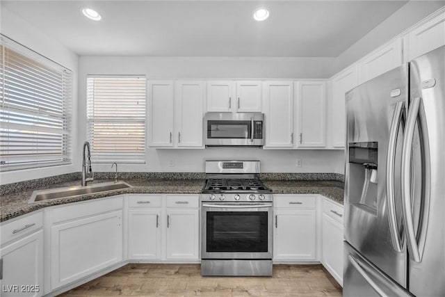 kitchen with stainless steel appliances, white cabinetry, sink, and light hardwood / wood-style floors