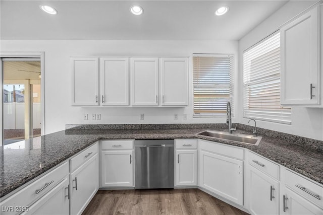 kitchen featuring sink, light wood-type flooring, stainless steel dishwasher, dark stone counters, and white cabinets