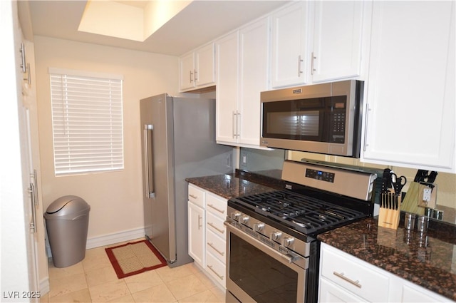 kitchen with appliances with stainless steel finishes, dark stone countertops, white cabinets, and light tile patterned floors