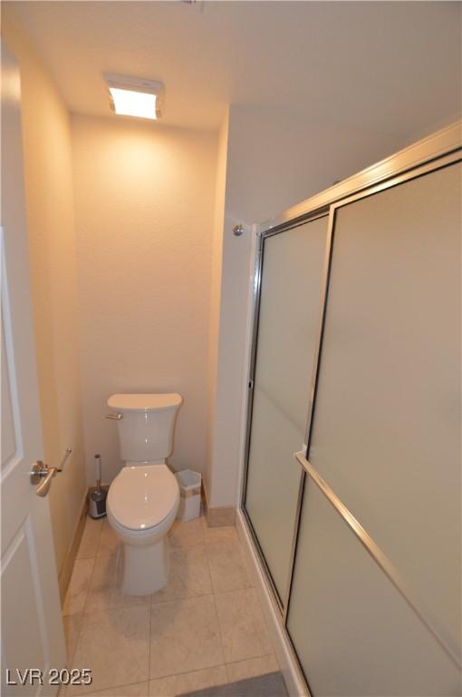 bathroom with tile patterned floors, toilet, and a shower with door