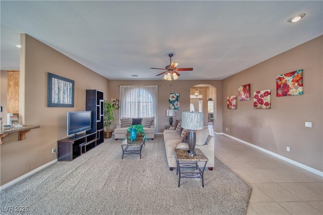 living area featuring arched walkways, light tile patterned floors, a ceiling fan, and baseboards