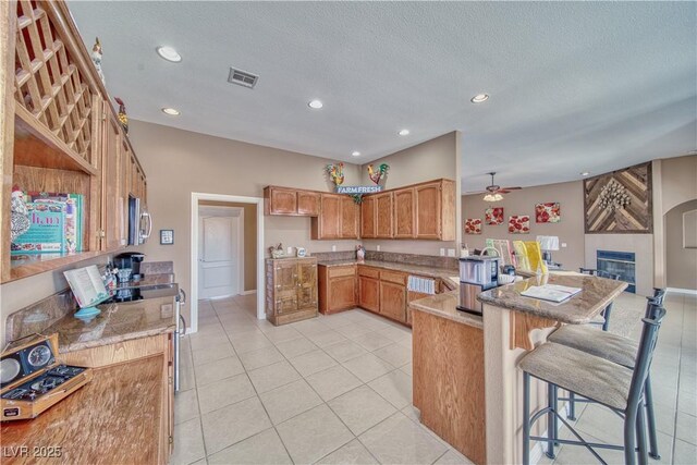 kitchen featuring a breakfast bar area, ceiling fan, a textured ceiling, light tile patterned flooring, and kitchen peninsula