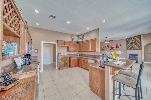 kitchen featuring visible vents, ceiling fan, a breakfast bar, a peninsula, and a fireplace