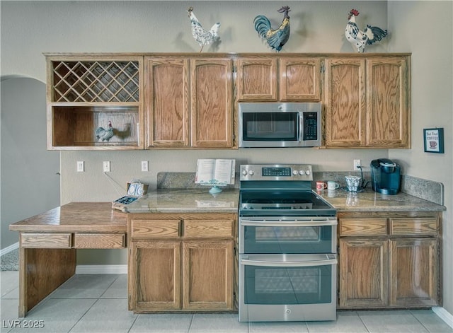 kitchen with appliances with stainless steel finishes, light countertops, brown cabinetry, and light tile patterned floors