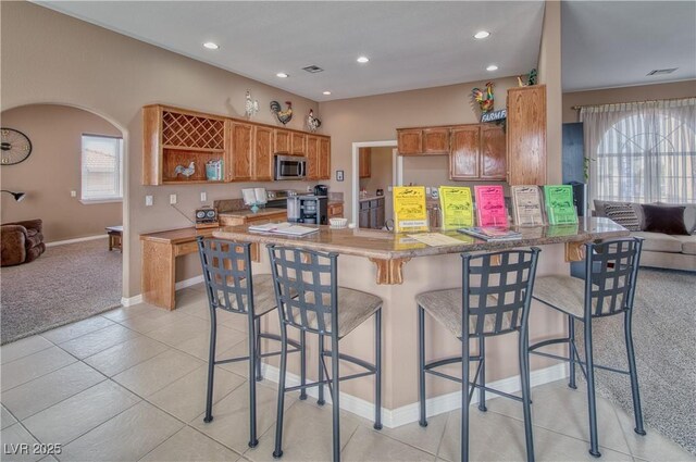 kitchen with appliances with stainless steel finishes, light tile patterned floors, a kitchen bar, and kitchen peninsula