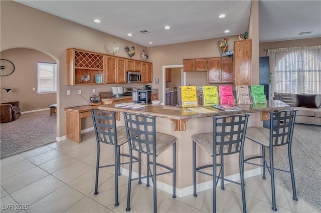 kitchen with arched walkways, appliances with stainless steel finishes, brown cabinets, a peninsula, and light countertops