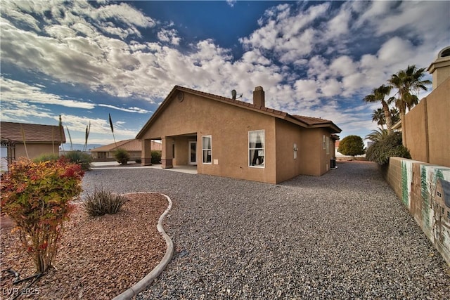 rear view of property featuring a patio, fence, a tiled roof, and stucco siding