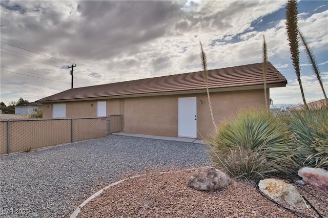 back of property with a tiled roof, fence, and stucco siding