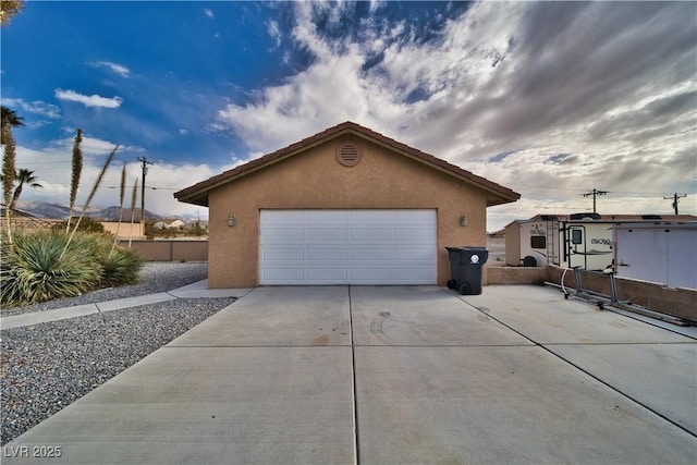 view of side of property featuring an outbuilding, concrete driveway, fence, and stucco siding