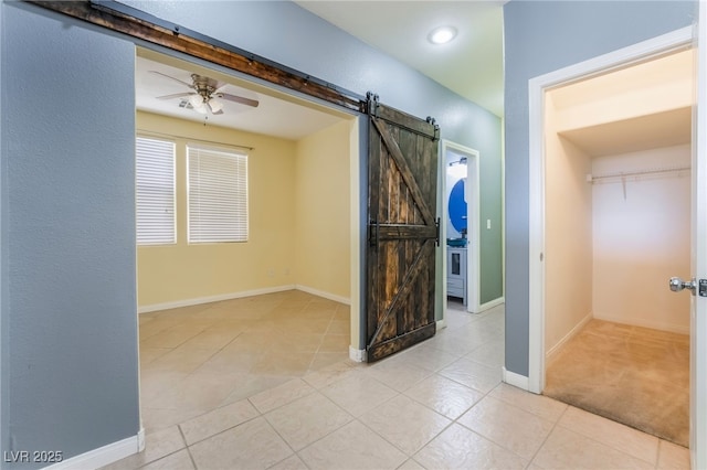 empty room with tile patterned floors, ceiling fan, baseboards, and a barn door