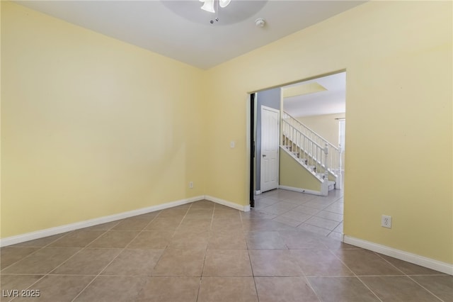 tiled spare room featuring baseboards, stairway, and ceiling fan